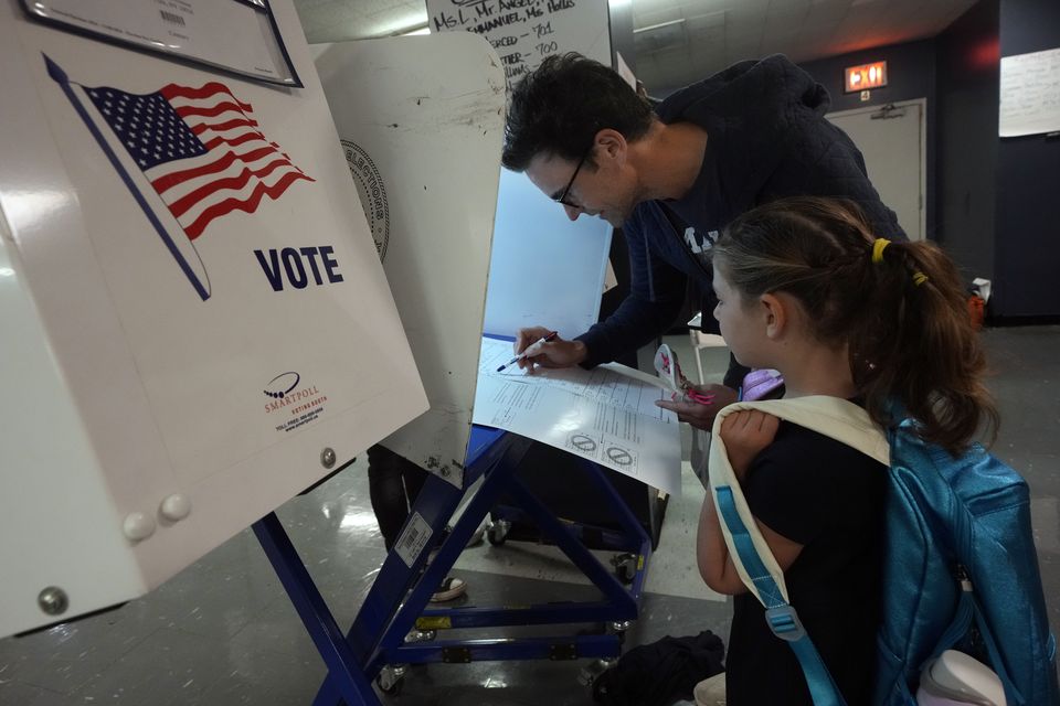 Benay Gould, seven, watches as her father Charles Herschel marks his ballot at PS M811, The Mickey Mantle School in New York (Richard Drew/AP)