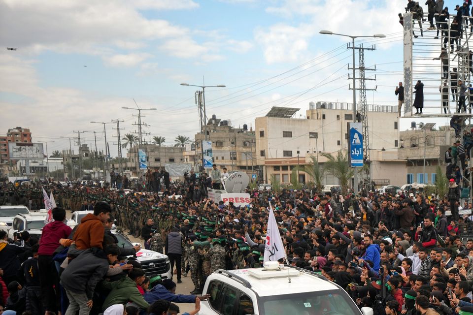 Palestinians gather as Hamas fighters escort Red Cross vehicles carrying the captives in Deir al-Balah, central Gaza Strip (Abdel Kareem Hana/AP)