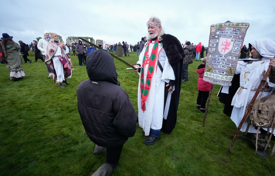 Arthur Pendragon ‘knights’ a member of the public as they take part in the Stonehenge gathering (Andrew Matthews/PA)