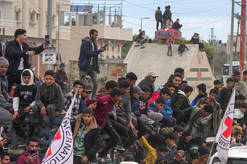 Palestinians gather as Hamas fighters escort Red Cross vehicles (Abdel Kareem Hana/AP)