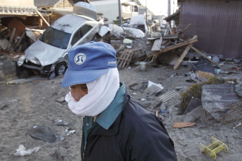A man, with his face covered to protect against dust, looks out at the damage Monday, March 14, 2011, in Yotsukura, Japan, three days after a giant quake and tsunami struck the country's northeastern coast. (AP Photo/Gregory Bull)