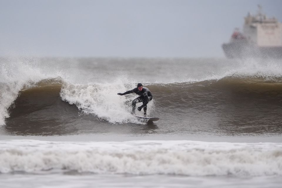 A surfer catches a wave in the wind at Tynemouth Longsands on the north east coast of England (Owen Humphreys/PA)