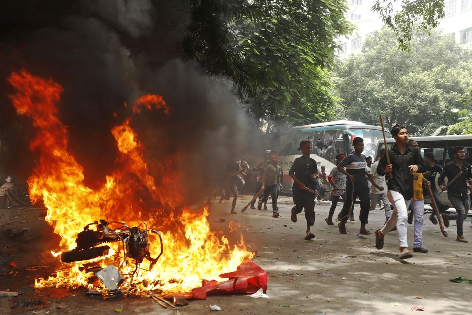 Men run past a burning vehicle inside the Bangabandhu Sheikh Mujib Medical University Hospital, set on fire by protesters during a rally against Sheikh Hasina (AP)