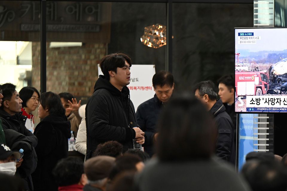 Family members of the passengers on a plane which burst into flames watch a TV news programme at Muan International Airport (Park Ki-woong/Newsis via AP/PA)