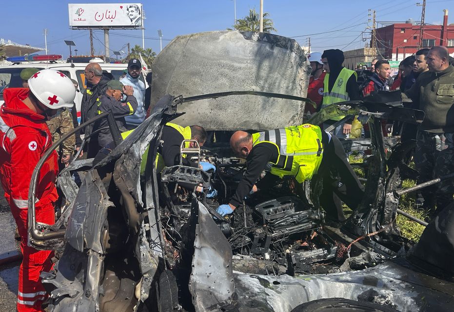 Civil Defence workers inspect the remains of a burned car in the Lebanese port city of Sidon (AP)