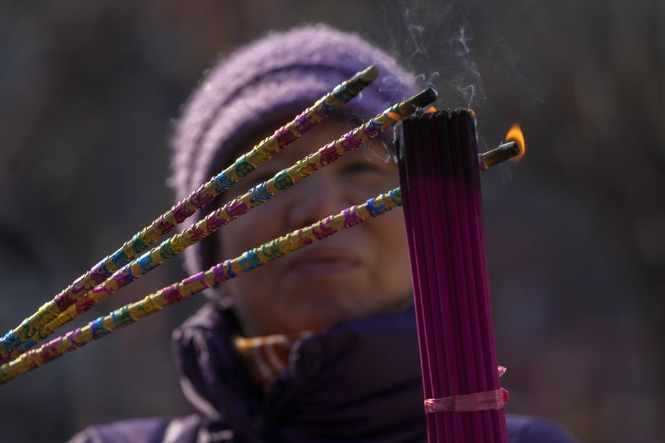 A woman lights incense sticks with prosperity wordings as she offers a prayer on the first day of the Chinese Lunar New Year at the Dongyue Temple in Beijing (Andy Wong/AP)