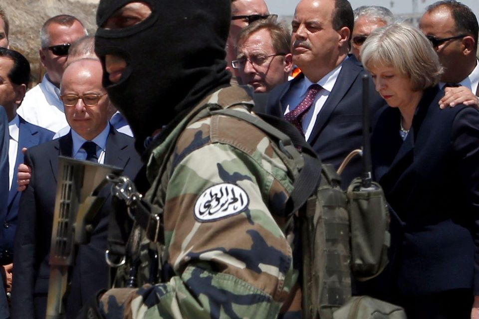 A hooded Tunisian police officer stands guard as British Home Secretary Theresa May, right, Tunisian Interior Minister Mohamed Najem Gharsalli, 2nd right, and French Interior Minister Bernard Cazeneuve, left, pay respect to the victims of Friday's shooting attack on the beach in front of the Imperial Marhaba hotel in the Mediterranean resort of Sousse, Tunisa, Monday, June 29, 2015. Seven people are being interrogated in Tunisia's capital in the investigation into a deadly beach resort attack that killed 38 people, according to a person with knowledge of the investigation. (AP Photo/Abdeljalil Bounhar)