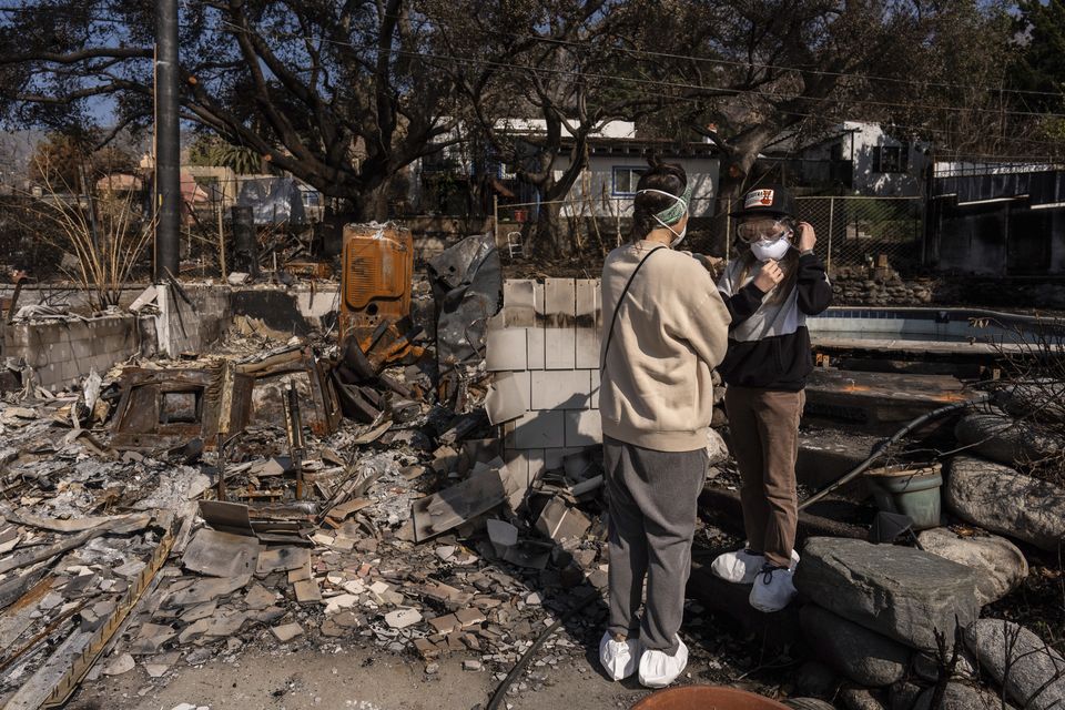 Eaton Fire evacuees Ceiba Phillips, 11, right, adjusts his mask as he and his mother, Alyson Granaderos, stand next to what remains of their in-law suite during Ceiba’s first visit to their home since the fire in Altadena (AP/Jae C. Hong)