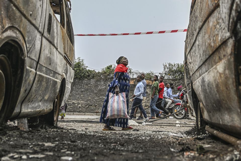 Residents walk by charred vehicles in Goma (Moses Sawasawa/AP)