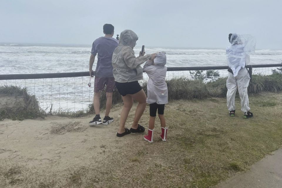 People stand at the beach in high winds as the remnants of cyclone Alfred arrives on the Gold Coast (John Pye/AP)