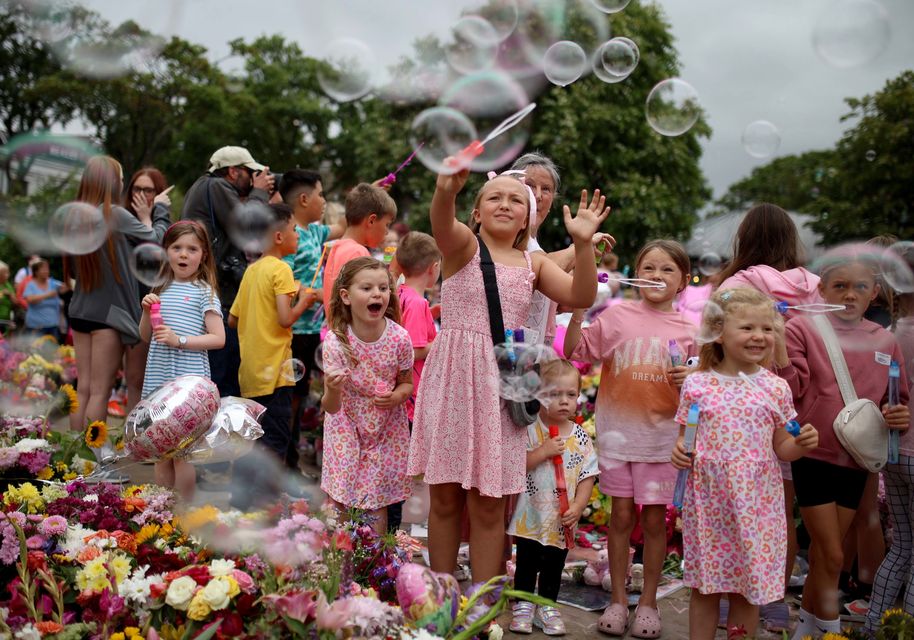 Young children play with bubble wands among floral tributes (Ryan Jenkinson/PA)