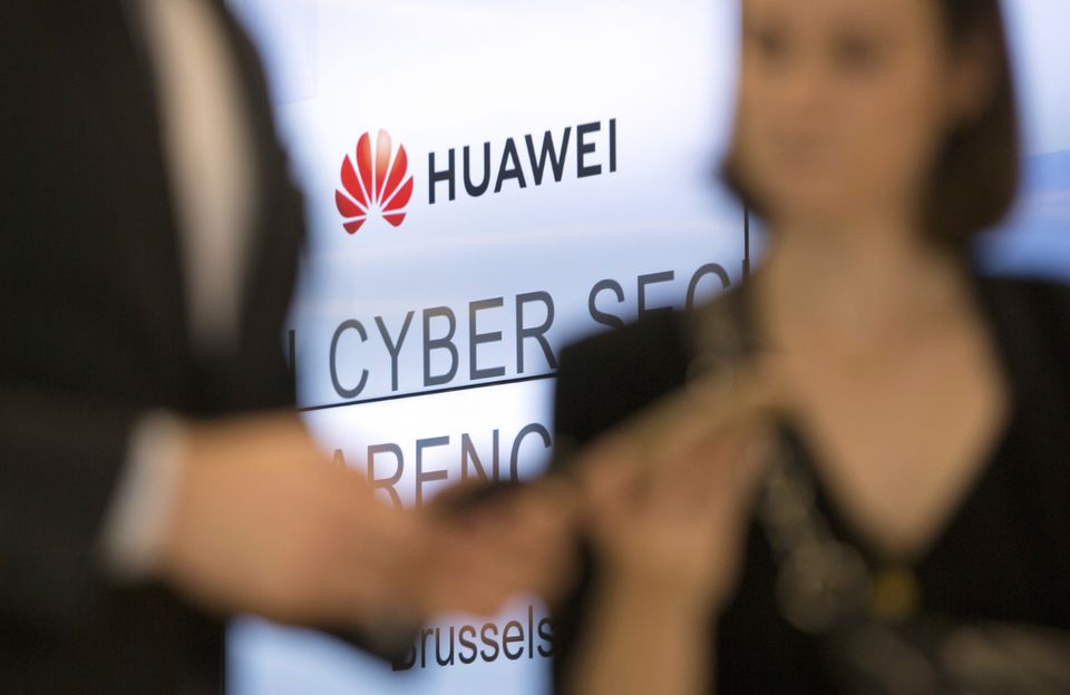 People looking at their phones in front of the Huawei logo during a conference in Brussels (Virginia Mayo/AP)