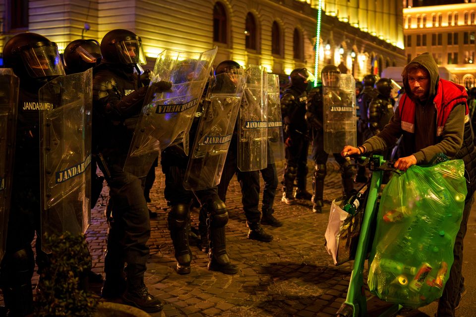 A man walks by riot police blocking a street following clashes with supporters of Calin Georgescu (Vadim Ghirda/AP)