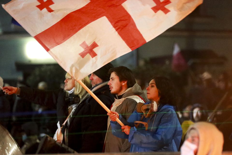 A demonstrator holds a Georgian national flag outside the parliament’s building in Tbilisi (AP Photo/Zurab Tsertsvadze)