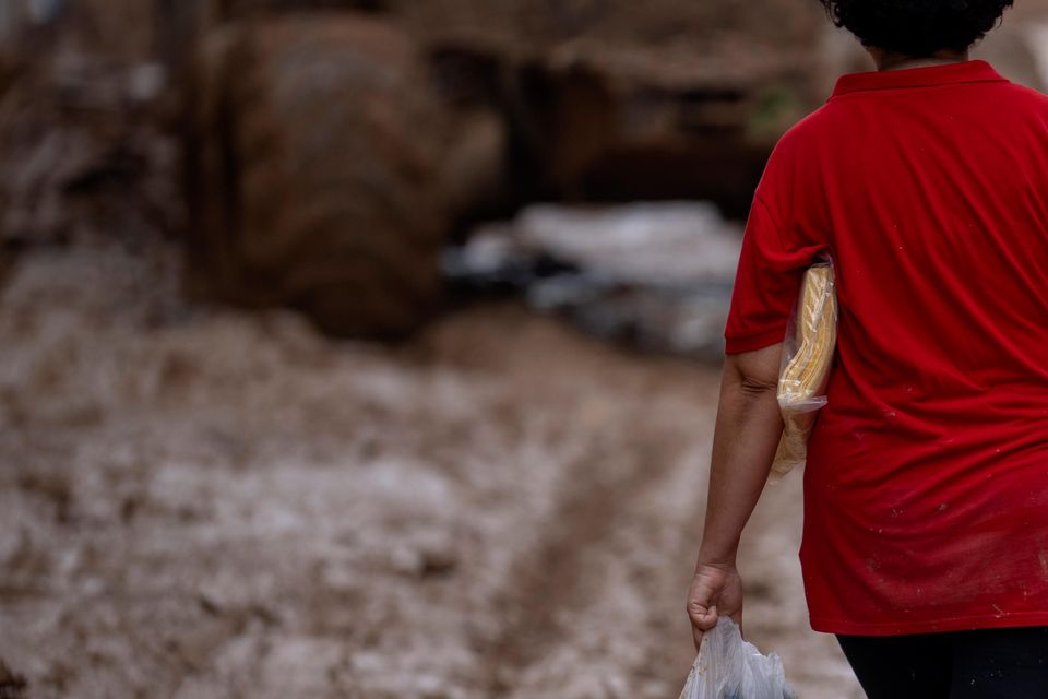 A woman carrying water and boots walks through the muddy streets after the floods in in Masanasa, Valencia, Spain (Emilio Morenatti/AP)