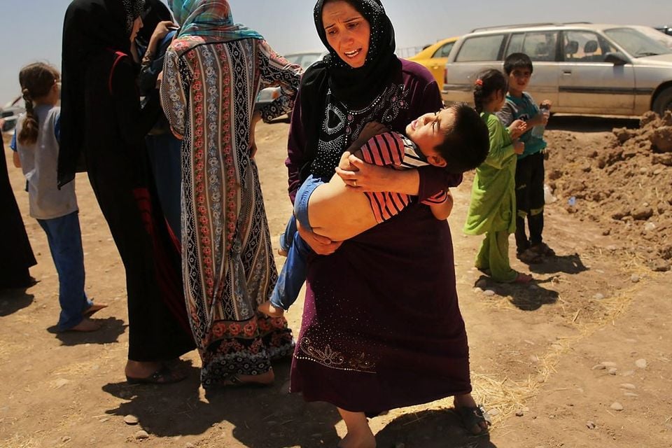 An Iraqi woman holds her exhausted son as over 1000 Iraqis who have fled fighting in and around the city of Mosul and Tal Afar wait at a Kurdish checkpoint in the hopes of entering a temporary displacement camp on July 1, 2014 in Khazair, Iraq. The families, many with small and sick children, had no shelter and little water and food. The displacement camp Khazair is now home to an estimated 1,500 internally displaced persons (IDP's) with the number rising daily. Tens of thousands of people have fled Iraq's second largest city of Mosul after it was overrun by ISIS (Islamic State of Iraq and Syria) militants. Many have been temporarily housed at various IDP camps around the region including the area close to Erbil, as they hope to enter the safety of the nearby Kurdish region. (Photo by Spencer Platt/Getty Images)
