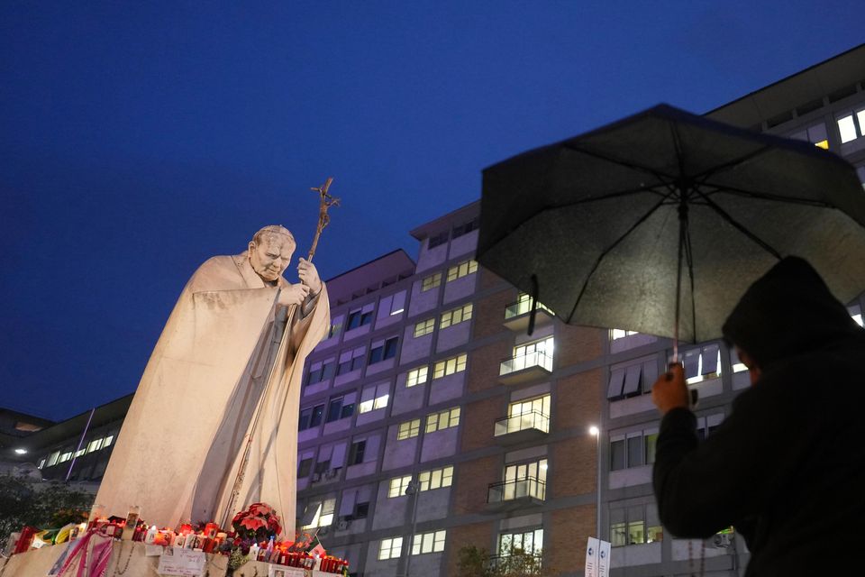 A man shelters from the rain as he prays for Pope Francis in front of the hospital where he is being treated (Kirsty Wigglesworth/AP)