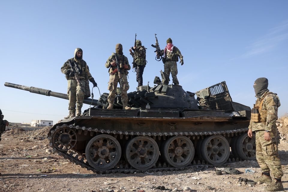 Syrian opposition fighters stand atop a seized military armoured vehicle on the outskirts of Hama, Syria (Ghaith Alsayed/AP)