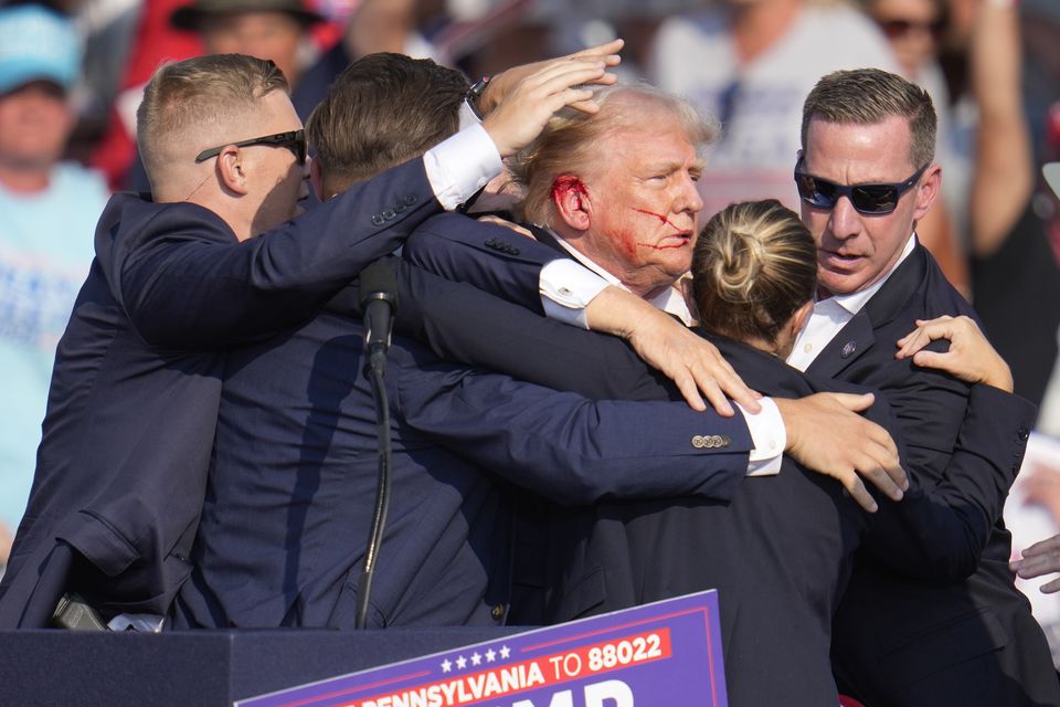 Donald Trump was surrounded by Secret Service agents as he left the stage with a bloodied ear following the attempt on his life (Gene J Puskar/AP)