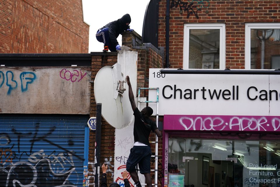 People remove a new artwork by Banksy from the roof of a shop in Peckham (Jordan Pettitt/PA)