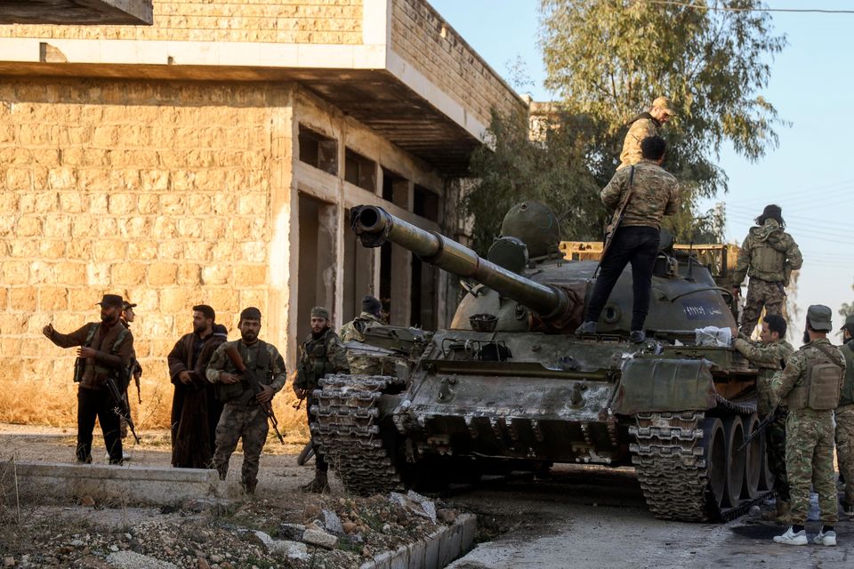 Opposition fighters stand on top of a captured Syrian army armoured vehicle in the town of Maarat al-Numan, south-west of Aleppo (Omar Albam/AP)