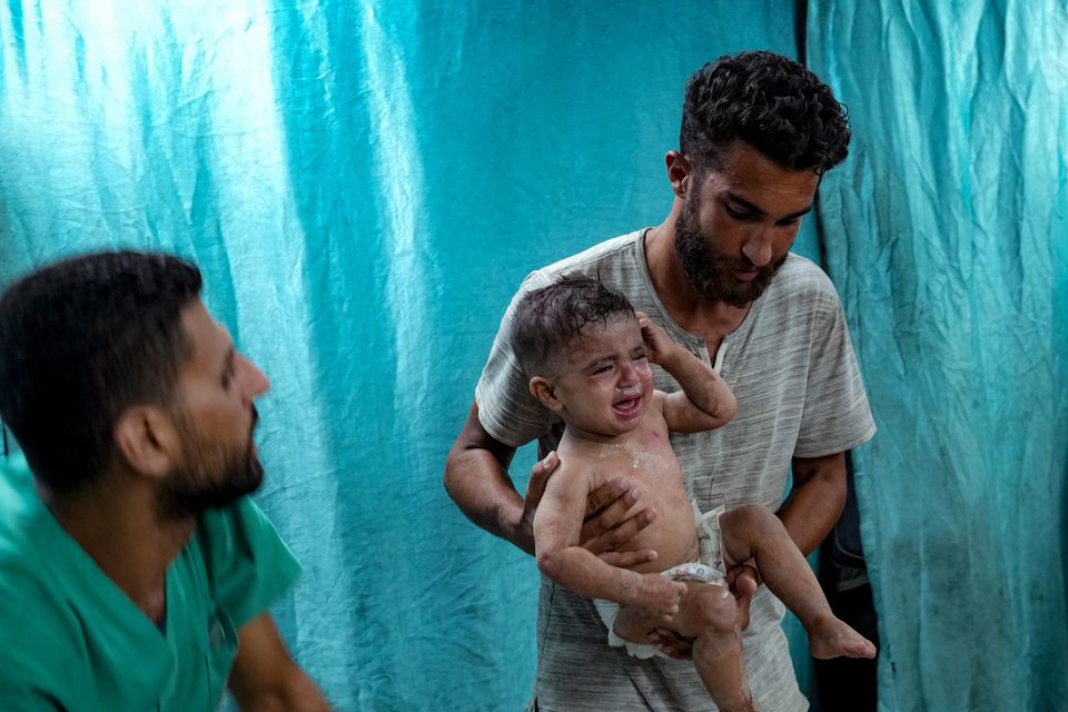 A Palestinian man holds a child wounded in the Israeli bombardment of the Gaza Strip in a hospital (Abdel Kareem Hana/AP)