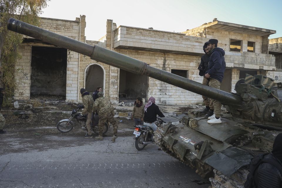 Syrian opposition fighters get on a motorcycle as others stand on top of a captured armoured vehicle in the town of Maarat al-Numan, south-west of Aleppo (Omar Albam/AP)