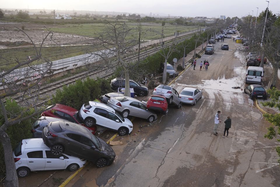 Residents walk next to cars piled up after being swept away by floods in Paiporta (Alberto Saiz/AP)