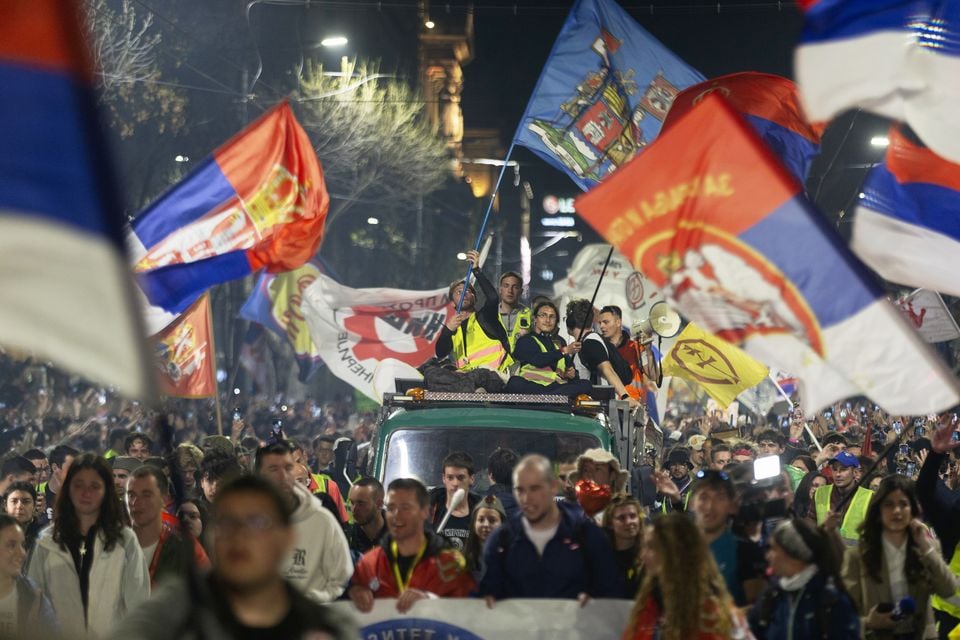 A large group led by students wave flags as they arrive at a protest (Marko Drobnjakovic/AP)