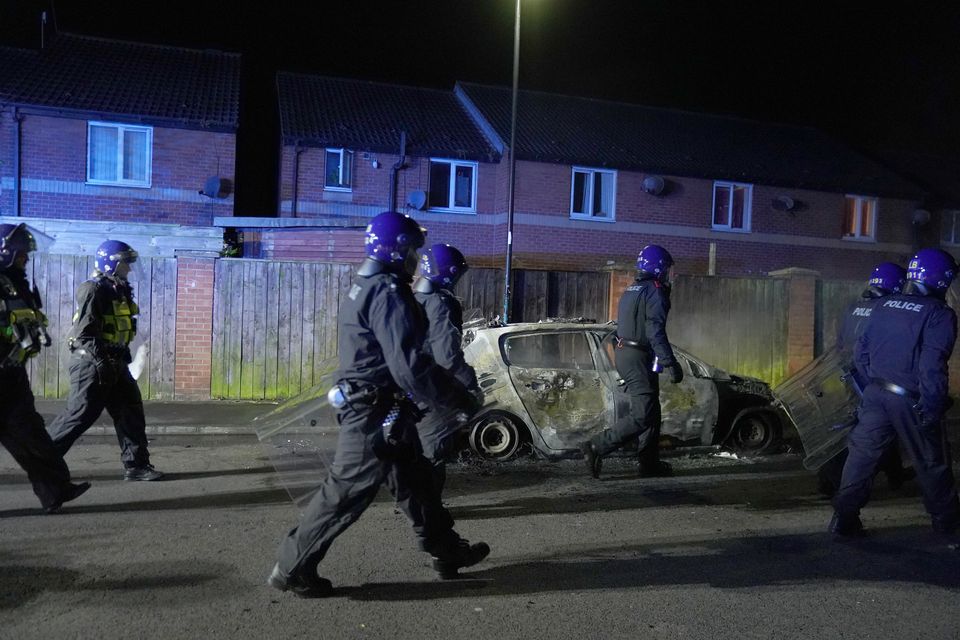 Police Officers walk past a burnt out police vehicle as they are deployed on the streets of Hartlepool following a violent protest (Owen Humphreys/PA)