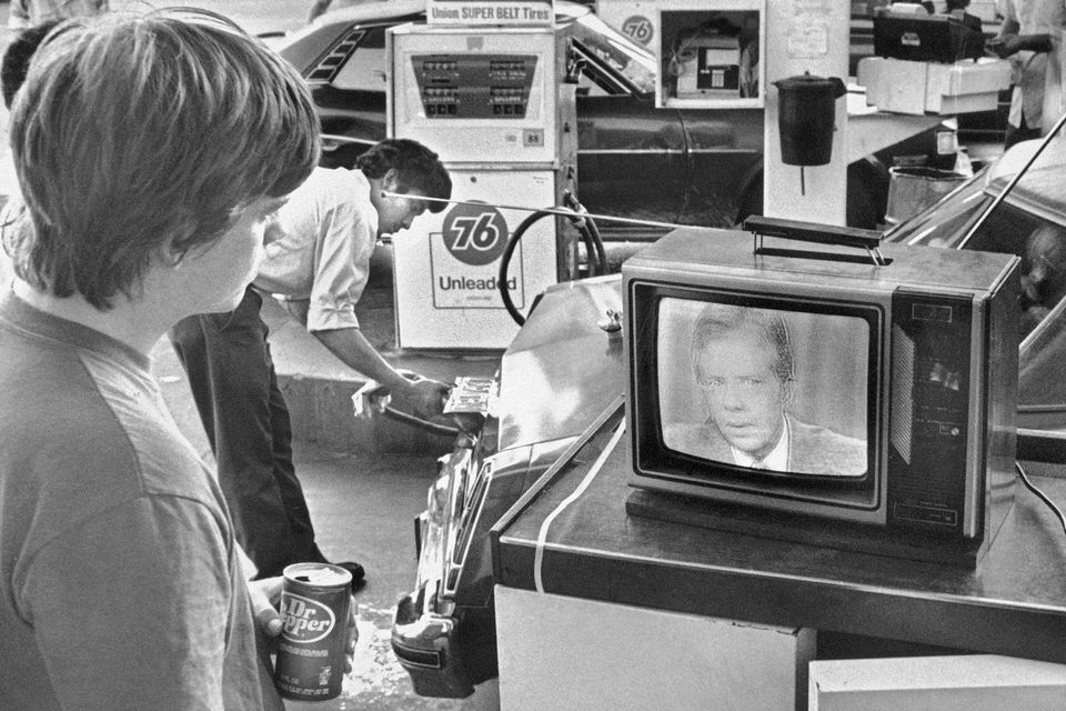 College student Chuck McManis watches President Jimmy Carter’s nationally televised energy speech from a service station in Los Angeles, as a petrol station attendant fills up a customer’s car (Mao/AP)