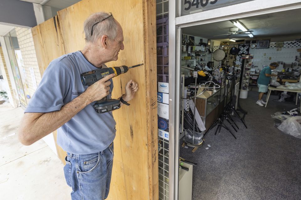 Jim Smetzer puts up boards as his wife Annette clears merchandise from their camera store in preparation for Hurricane Milton in New Port Richey (Mike Carlson/AP)