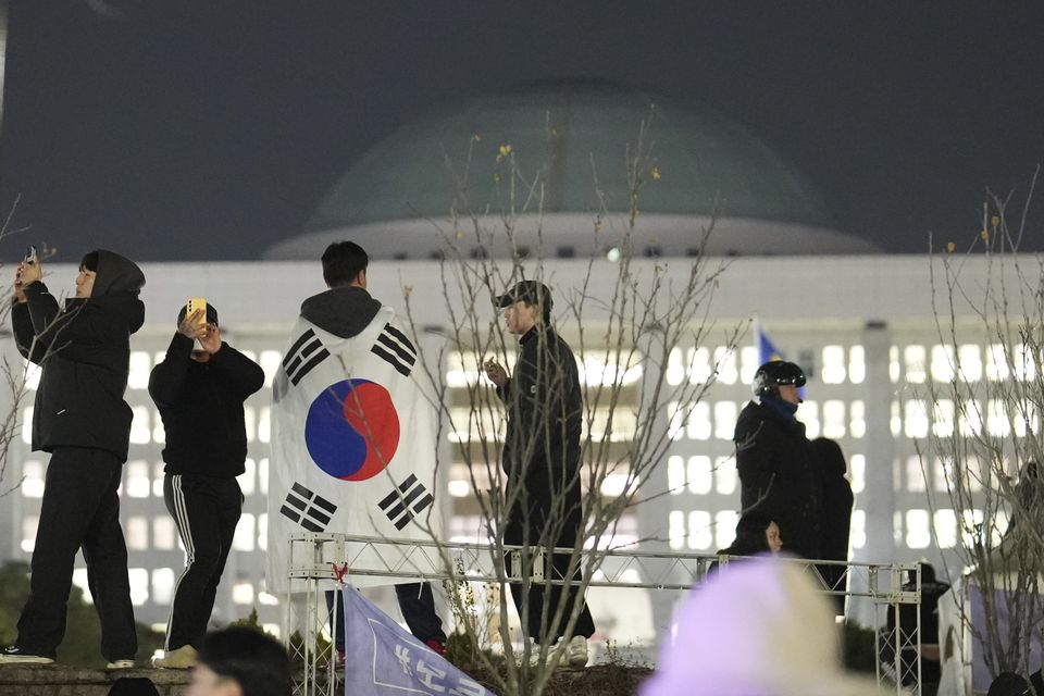 A man wearing a national flag stands on the wall of the National Assembly in Seoul (Lee Jin-man/AP)