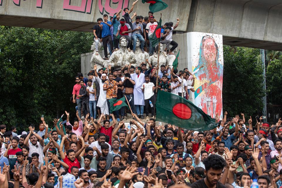 Protesters climb a public monument in Dhaka as they celebrate the news of Sheikh Hasina’s resignation as prime minister (Rajib Dhar/AP)