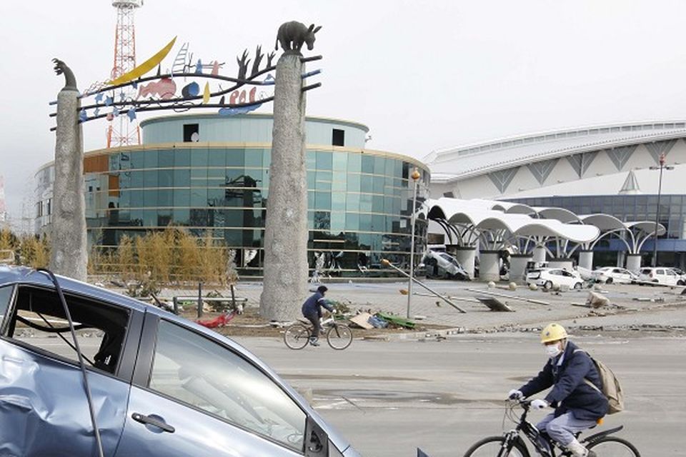 A man cycles past a wrecked car following the earthquake triggered tsunami at the port in Sendai, Japan (AP)