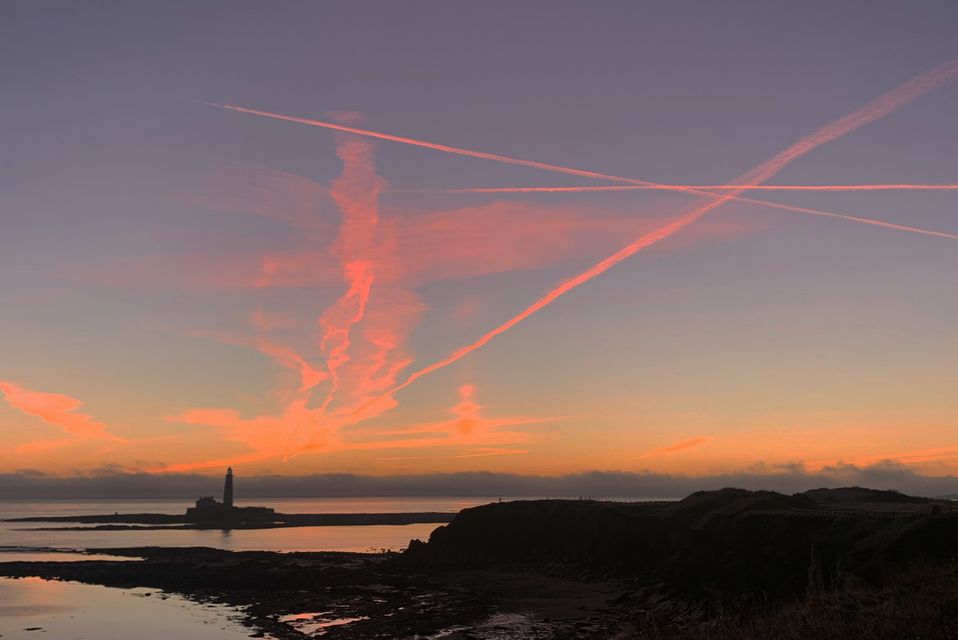 Plane contrails lit by the sun below the horizon before sunrise at St Marys Lighthouse in Whitley Bay off the North East coast (Owen Humphreys/PA)