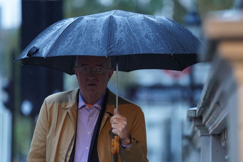 A man walks with an umbrella along Whitehall, London (PA)