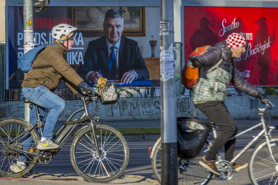 Cyclists ride past a poster of incumbent President Zoran Milanovic in Zagreb (AP)