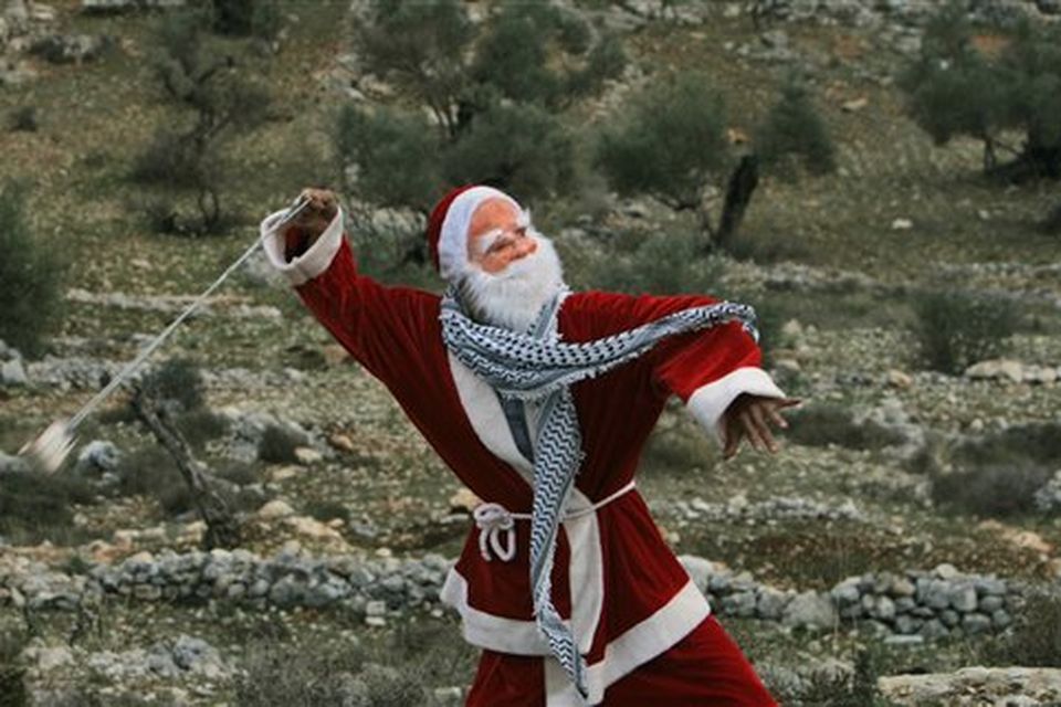 A Palestinian demonstrator dressed as Santa Claus uses a sling-shot to hurl stones at Israeli border police during a demonstration against Israel's separation barrier in the West Bank village of Bilin near Ramallah, Friday, Dec. 26, 2008. Israel says the barrier is necessary for security while Palestinians call it a land grab.(AP Photo/Muhammed Muheisen)