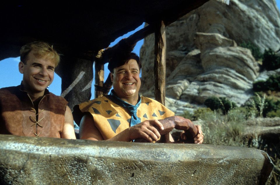 Rick Moranis and John Goodman riding together in a scene from the film The Flintstones