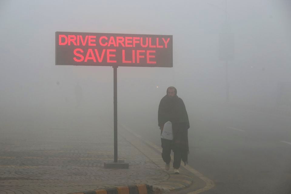 A man walks past a sign that reads “Drive carefully save life” in Peshawar, Pakistan (AP)