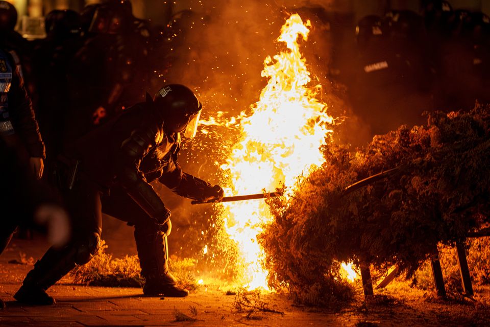 An officer attempts to extinguish a fire as supporters of Calin Georgescu protested in Bucharest (Vadim Ghirda/AP)