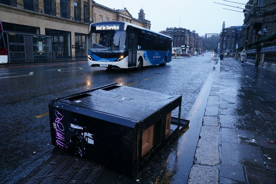 A bus drives around a bin that has fallen in the road, as drivers have been urged to avoid journeys unless necessary (Jane Barlow/PA)