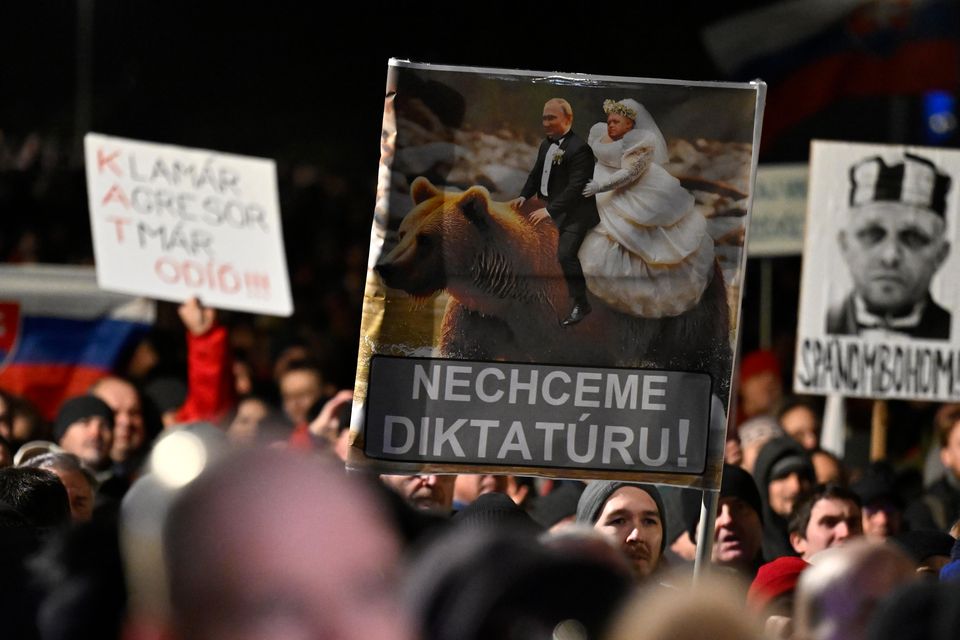 People hold up placards opposing Robert Fico (Denes Erdos/AP)