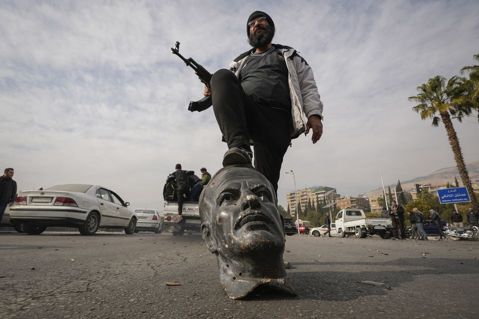 An opposition fighter steps on a broken bust of the late former Syrian president Hafez Assad (Hussein Malla/AP)