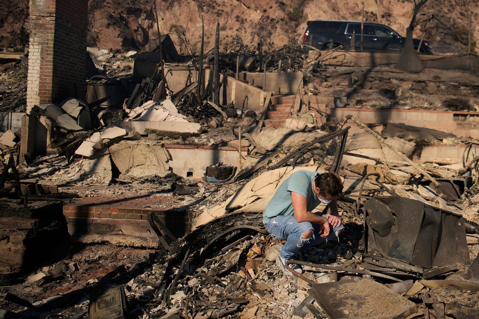 Luke Dexter kneels as he sifts through the remains of his father’s fire-ravaged beachfront property in the aftermath of the Palisades Fire (John Locher/AP)