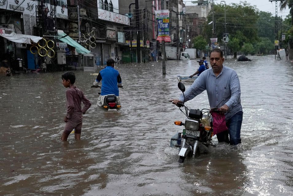 Motorcyclists drive through a flooded road caused by heavy monsoon rainfall in Lahore, Pakistan (KM Chaudary/AP)