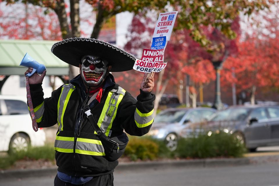 Boeing mechanic Eugenio, who preferred not to give a last name, sounds a bullhorn while holding a sign (Lindsey Wasson/AP)