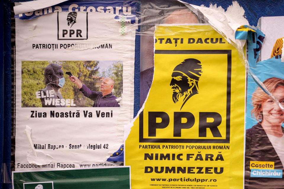 Posters of various political parties, one showing a man pointing a thermometer at a statue of Ellie Wiesel and reading “Our Day Will Come” a placed on a panel ahead of the country’s parliamentary elections (AP Photo/Andreea Alexandru)