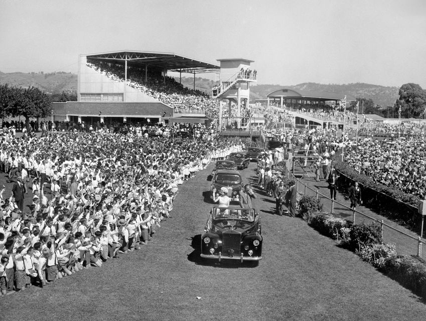 Queen Elizabeth II and the Duke of Edinburgh stand in an open Rolls Royce at Victoria Park racecourse in Adelaide, as 75,000 schoolchildren gave a rousing welcome in 1963 (PA)